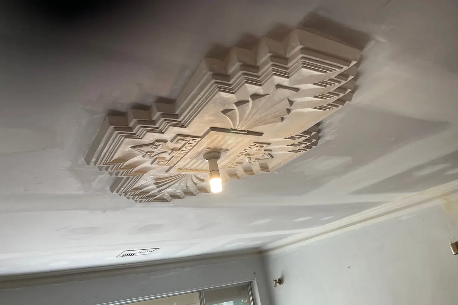 Art deco stepped plaster ceiling centrepiece with fresh setting plaster patched around it and a light fitting at the centre
