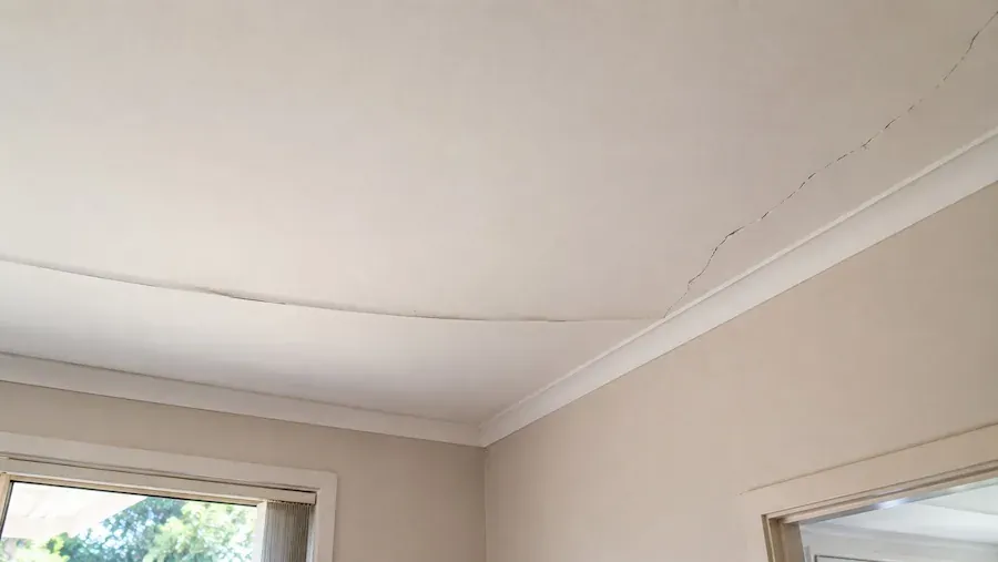 Bowed plaster ceiling with a crack running along the top edge of the cornice