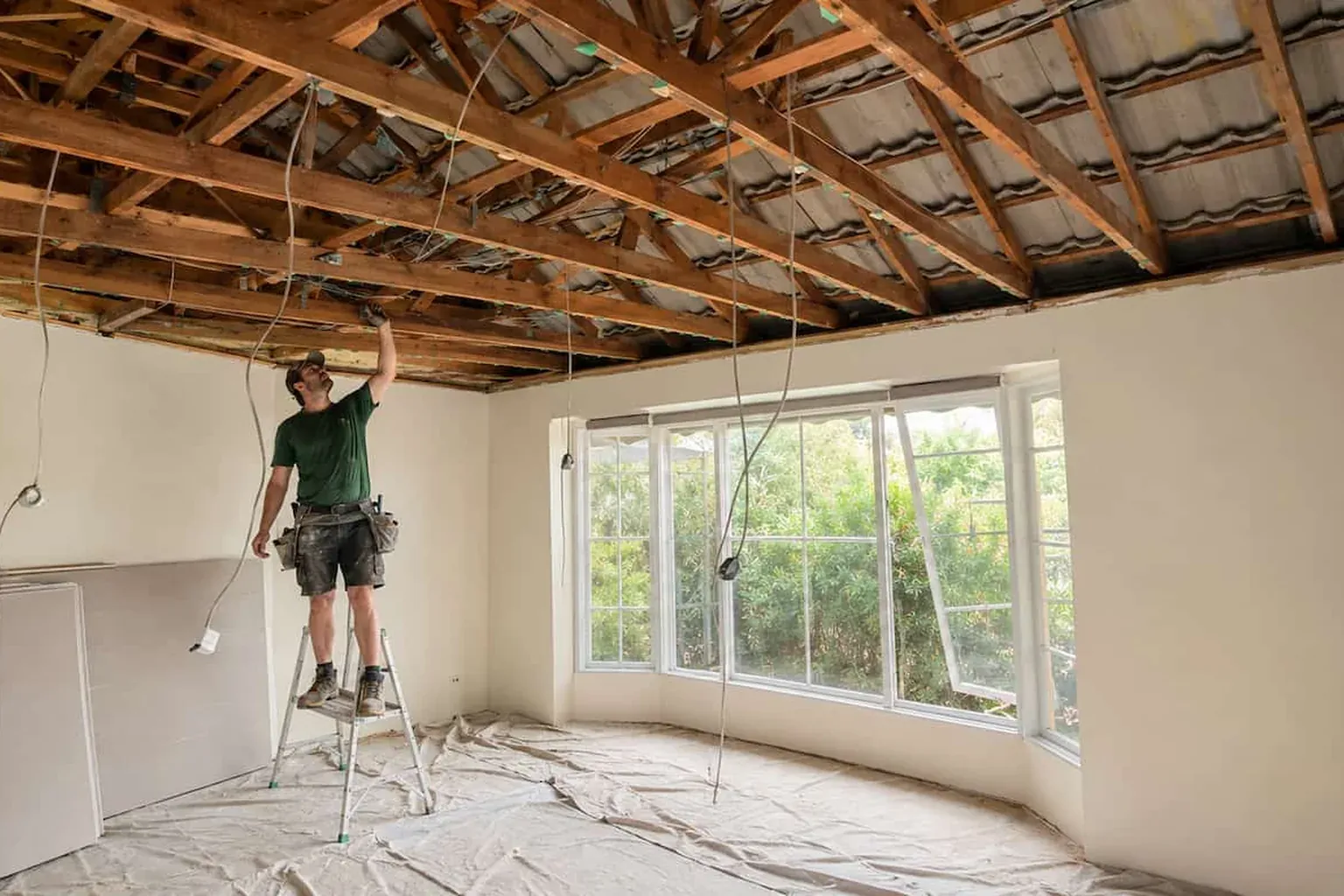 Room with the old ceiling removed and the roof timbers exposed, a ceiling fixer on a ladder preparing for new plasterboard