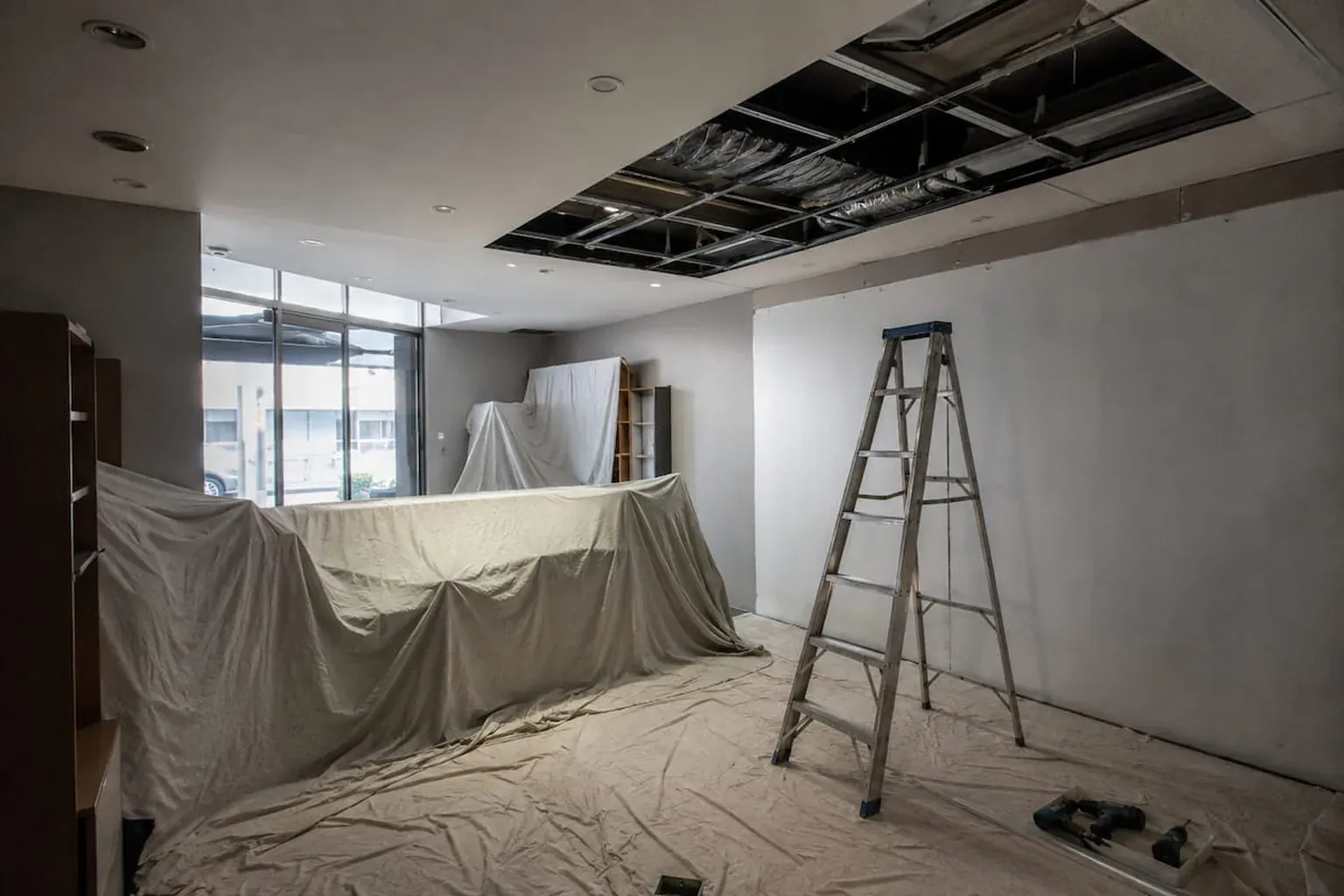 Commercial tenancy with the fit-out covered in drop sheets, a ladder set up and ceiling panels opened for access