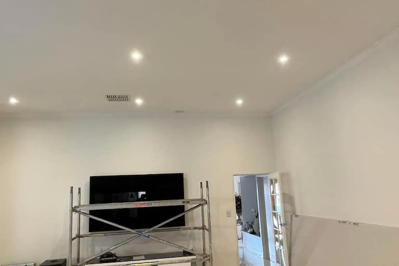 Finished white plasterboard ceiling with downlights, a mobile scaffold tower still standing in the living room