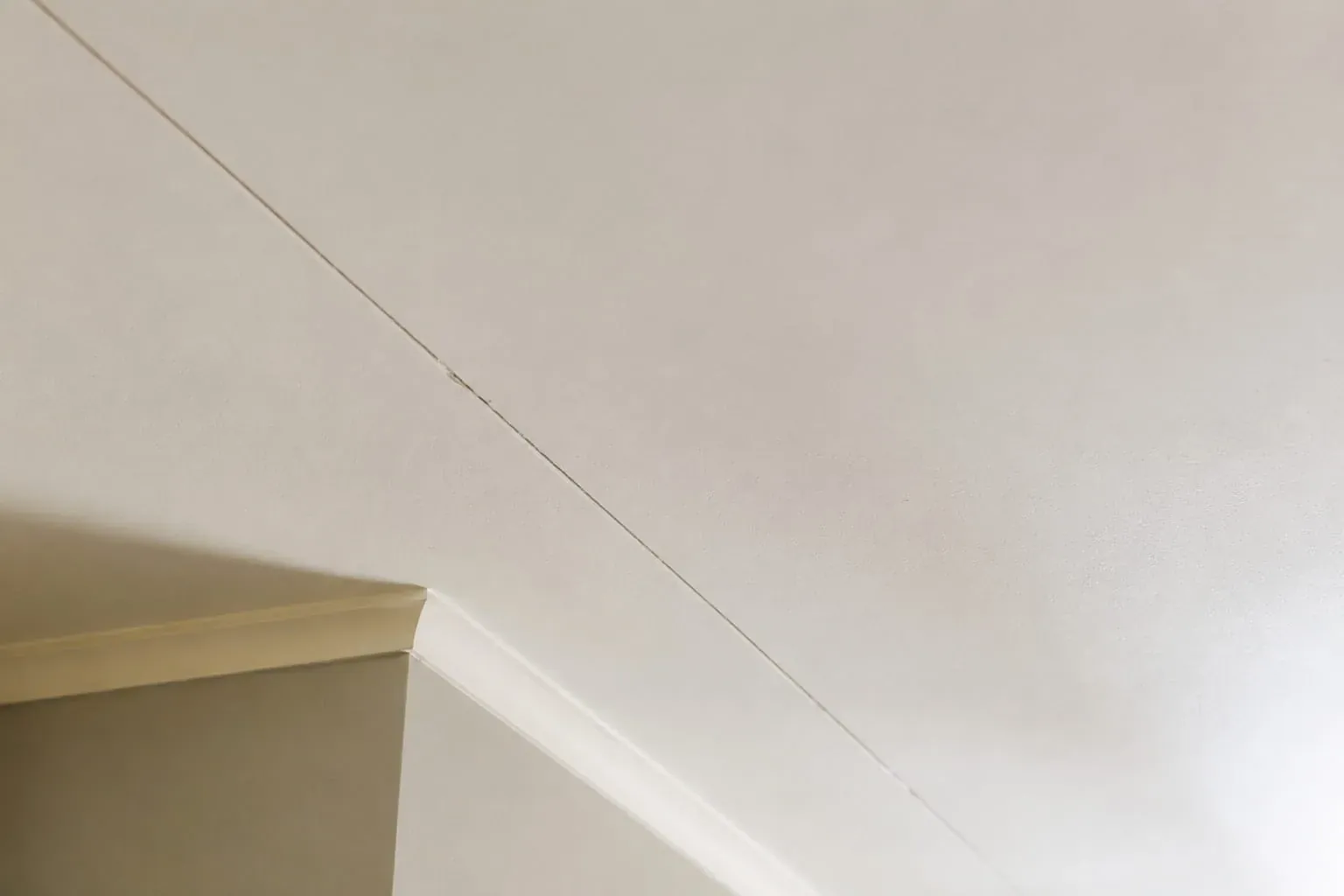 Close-up of a hairline crack running along a plasterboard sheet join in a white ceiling