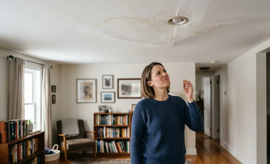 Homeowner looking up at a water stain spreading around a ceiling light fitting