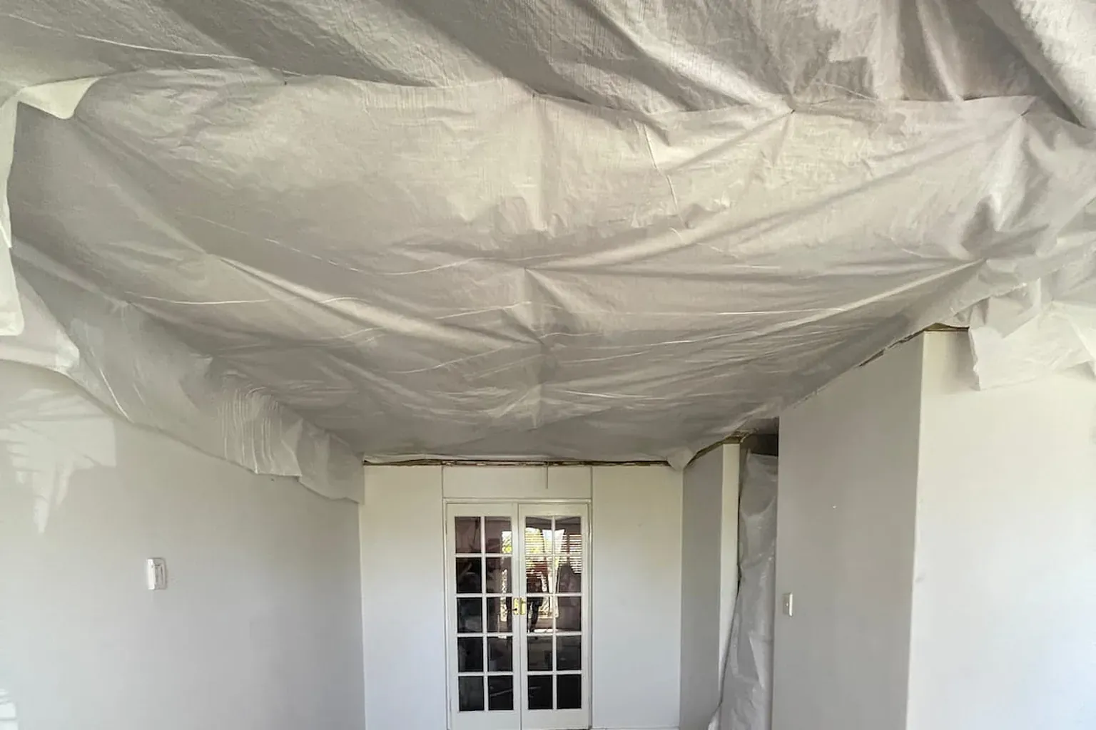 Damaged ceiling covered with plastic sheeting taped to the walls as a make-safe until the rebuild