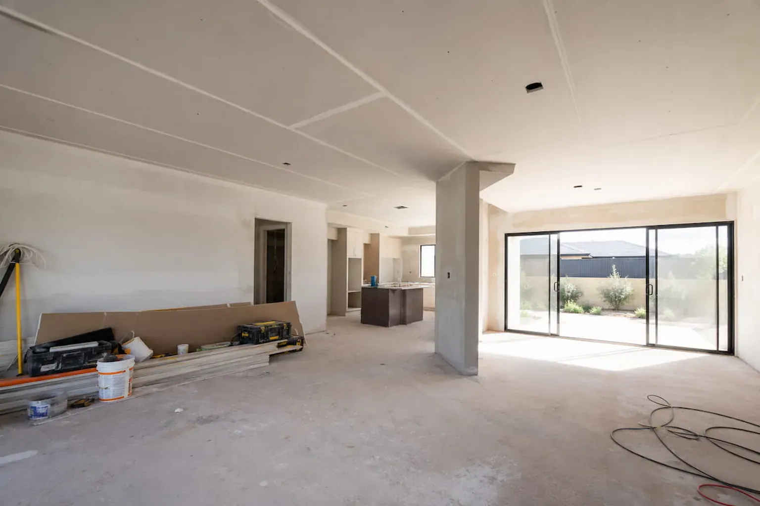 Open-plan living area mid-renovation with new plasterboard ceiling sheeted and set, bare concrete floor and tools below