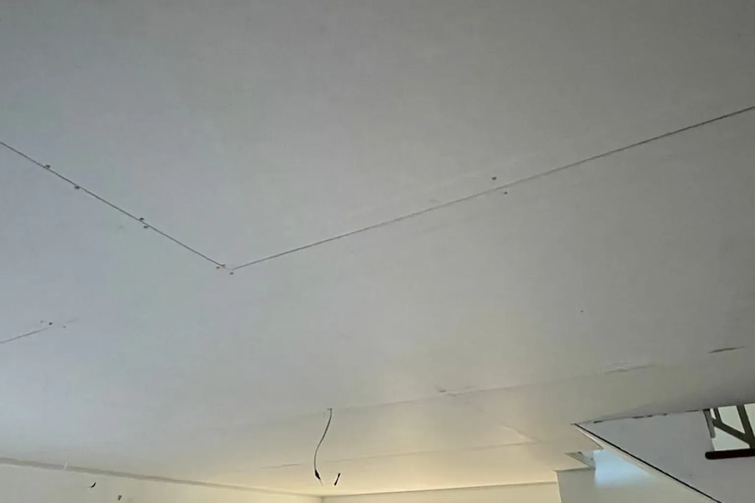 New plasterboard ceiling sheeted but not yet set, with light wiring hanging through the sheet