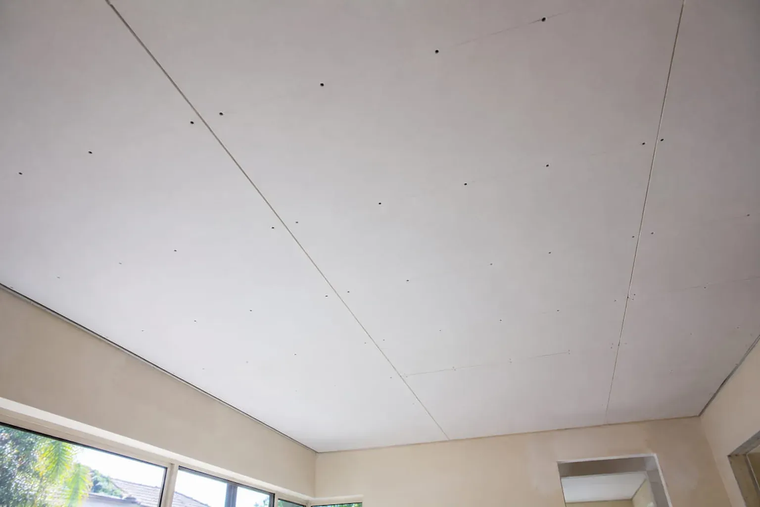 New plasterboard sheets on a raked ceiling, screw heads visible before setting