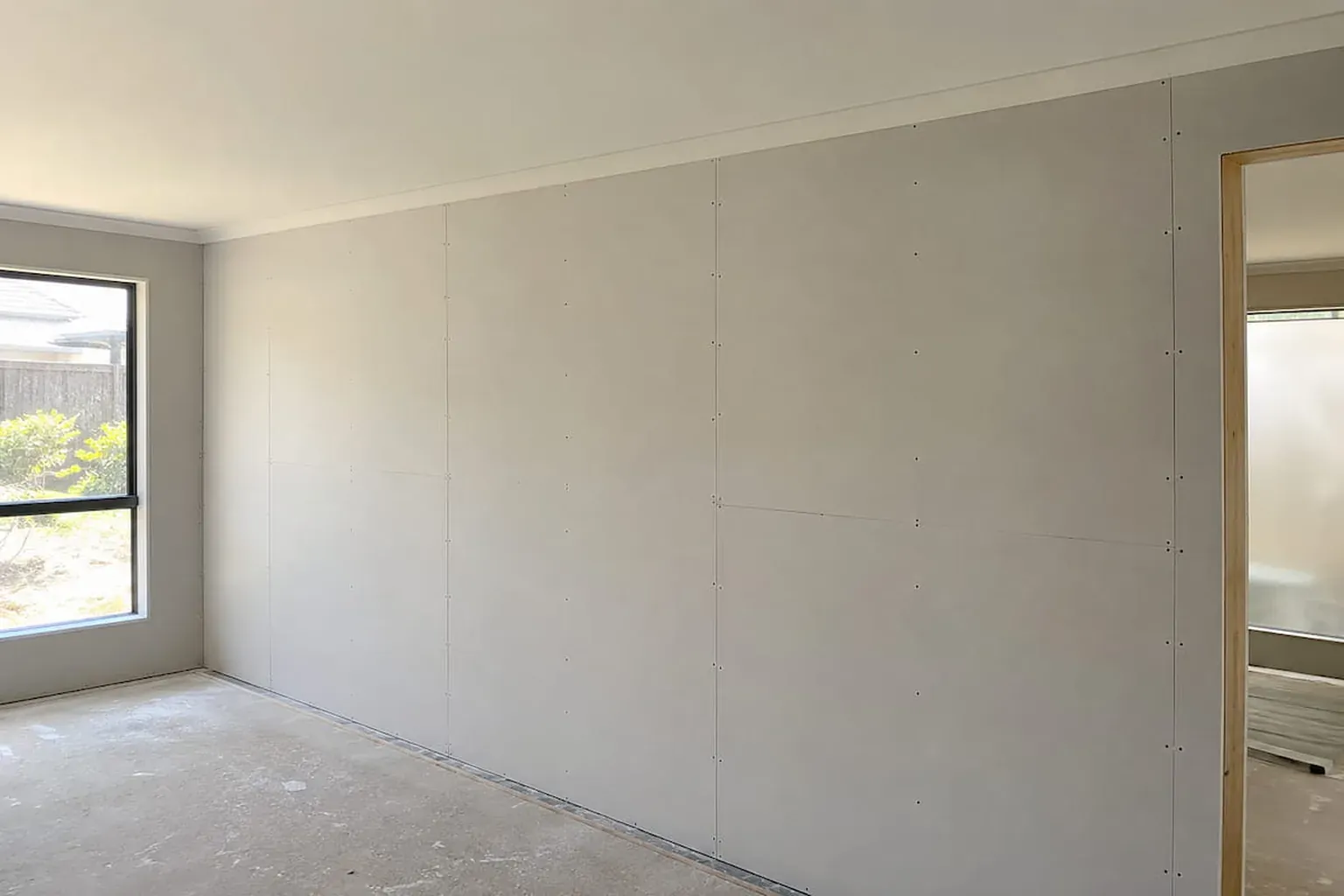 Extension room with walls and ceiling sheeted in new plasterboard, joins visible and floor still bare