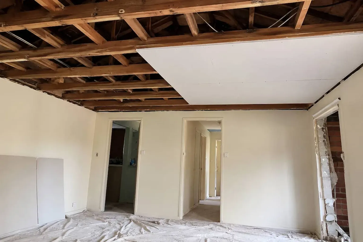 Room with the old ceiling removed, exposed timber joists and the first new plasterboard sheet fixed in place