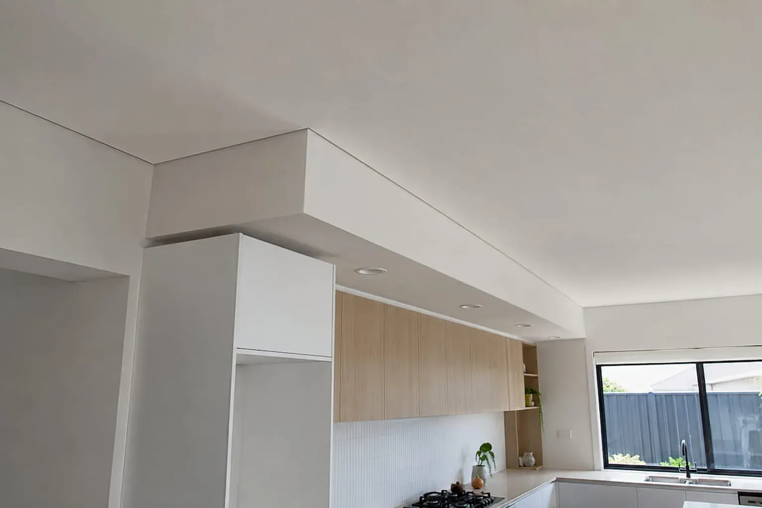 Finished plasterboard bulkhead running above a renovated kitchen with timber-look cabinetry