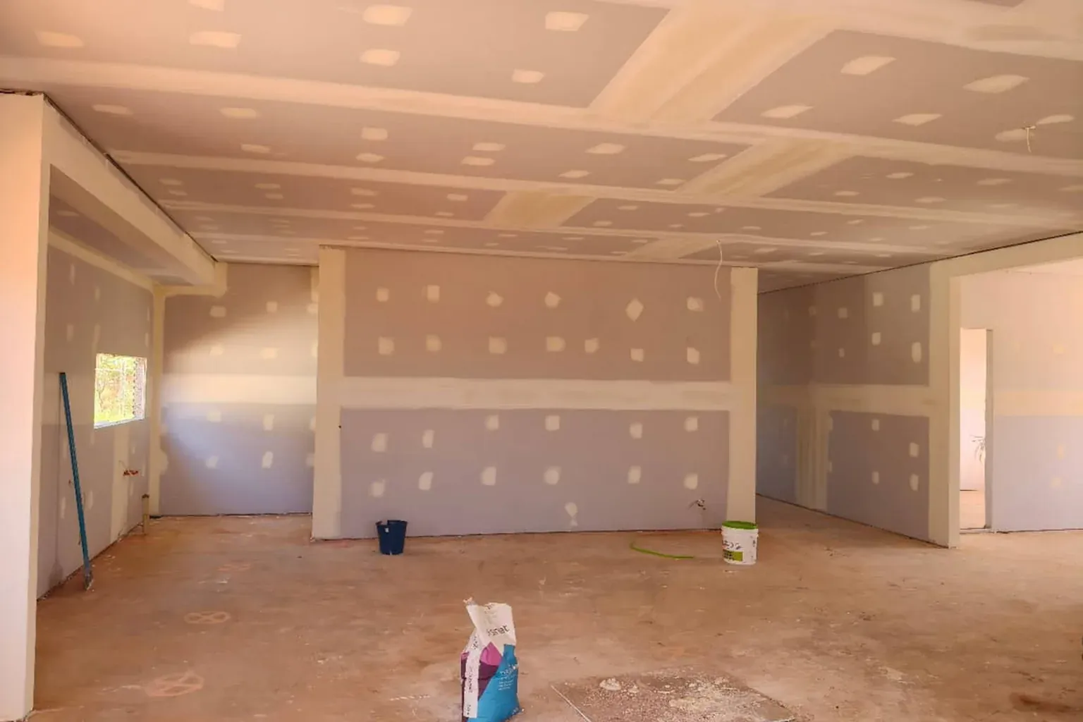 Room with walls and ceiling fully sheeted, every join and screw head set with plaster, ready for sanding