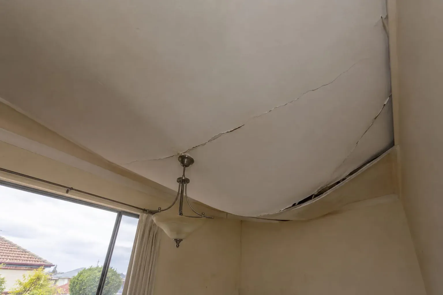 Ceiling sagging heavily and split along the join above a pendant light, close to coming down