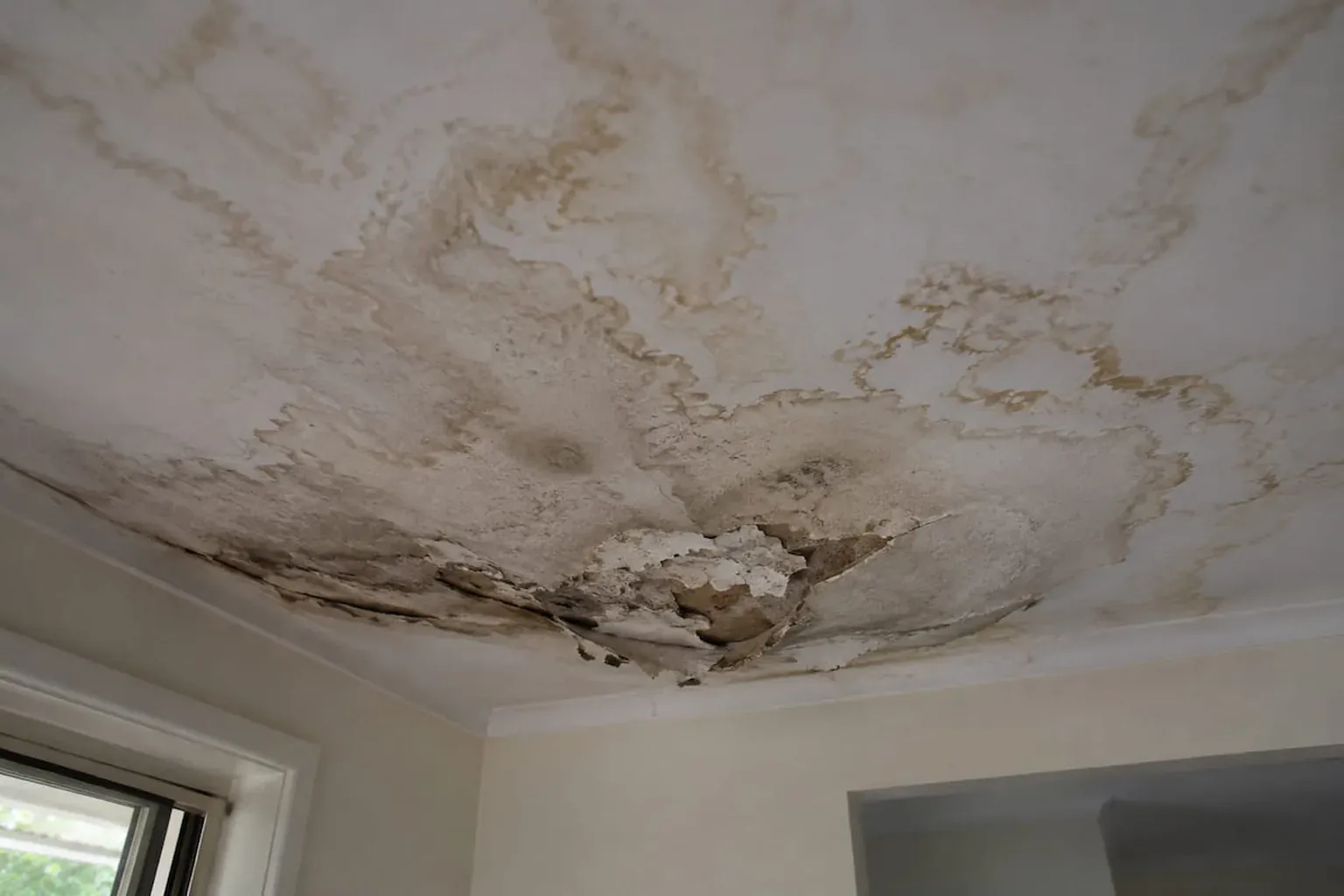 Severely water-damaged ceiling with staining spread across it and plaster breaking through in the middle