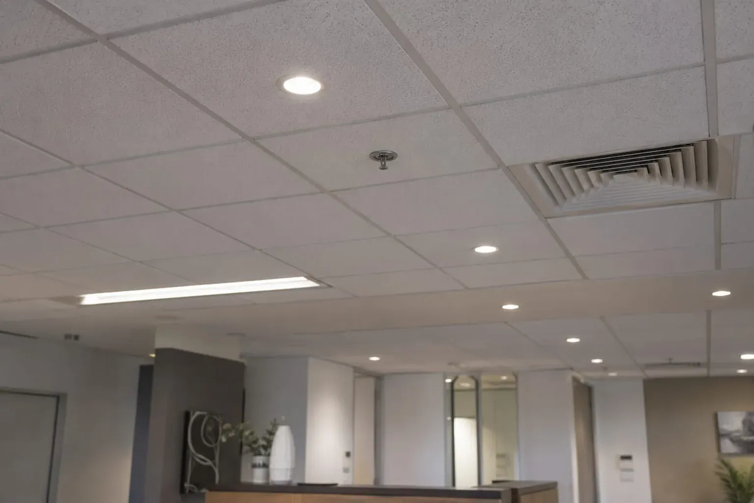 Ceiling tiles in an office reception with downlights, light panels and air diffusers fitted