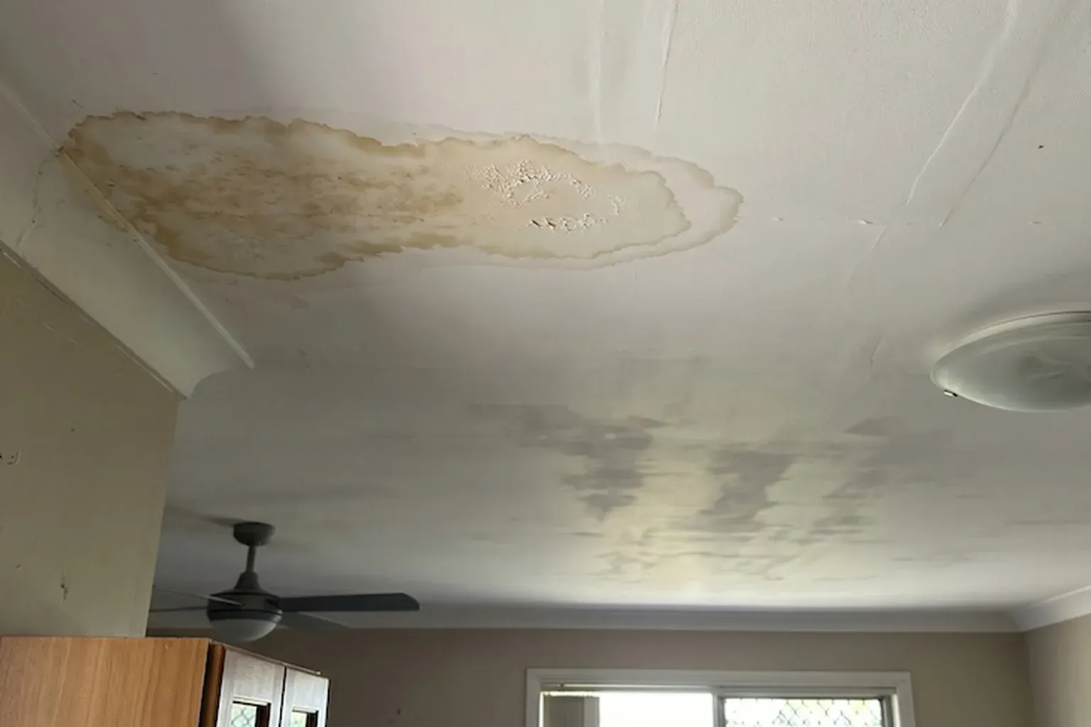 Brown water stain ring on a dining room ceiling beside a ceiling fan