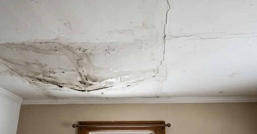Ceiling above a window with brown water staining, mould and a crack running through the stained area